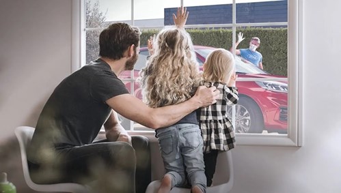 family waving out the window at a man